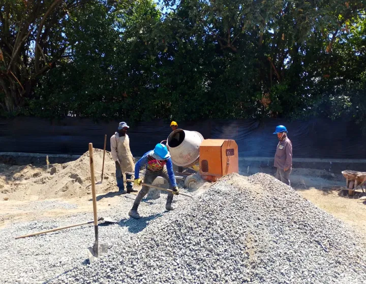 Cuadrilla mezclando concreto junto a la mezcladora y un montón de gravilla.