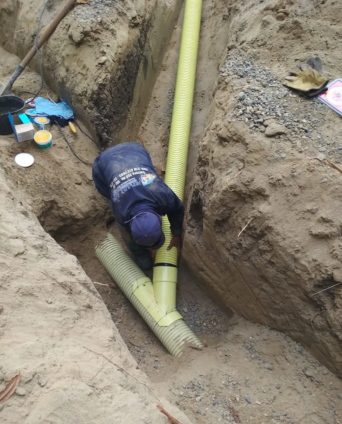 Operario empalmando tubería sanitaria en el fondo de una zanja.