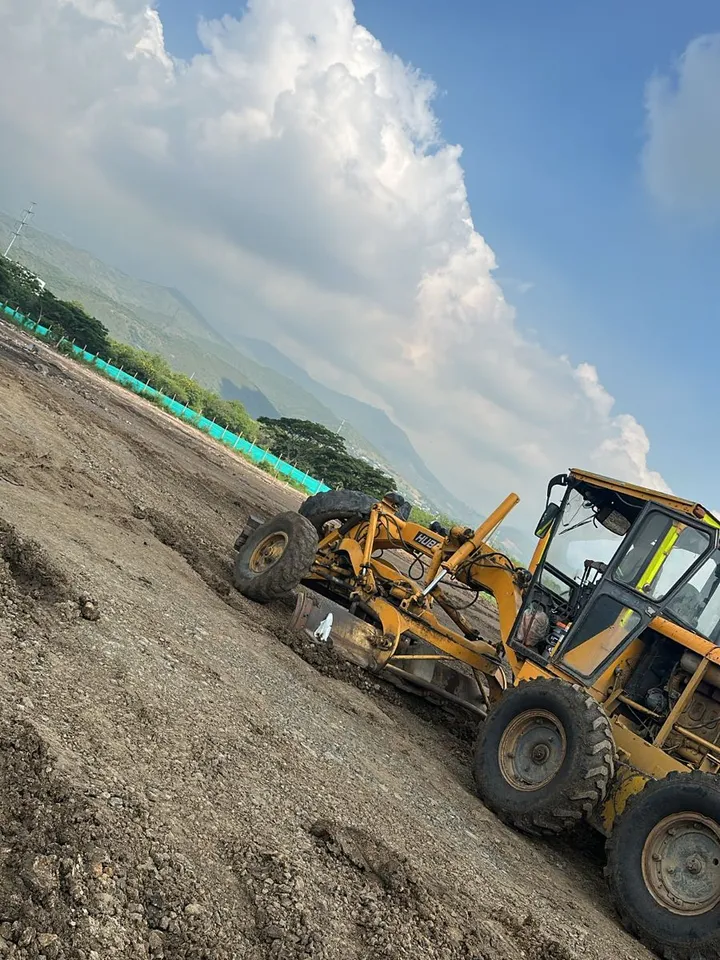 Motoniveladora nivelando terreno de la obra bajo un cielo con nubes de tormenta.